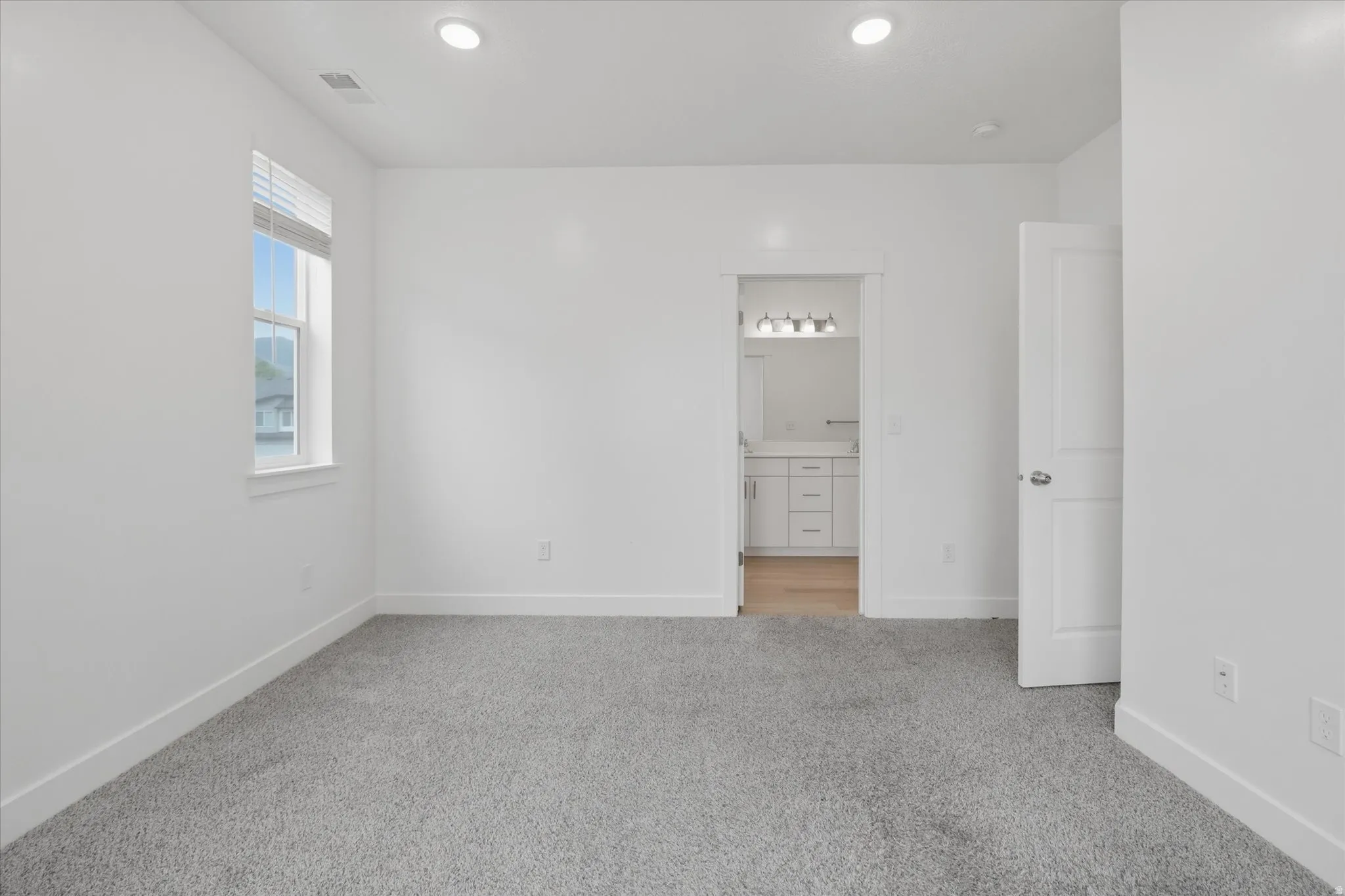 Spacious room featuring neutral carpeting, a large window with blinds, recessed ceiling lighting, and crisp white walls