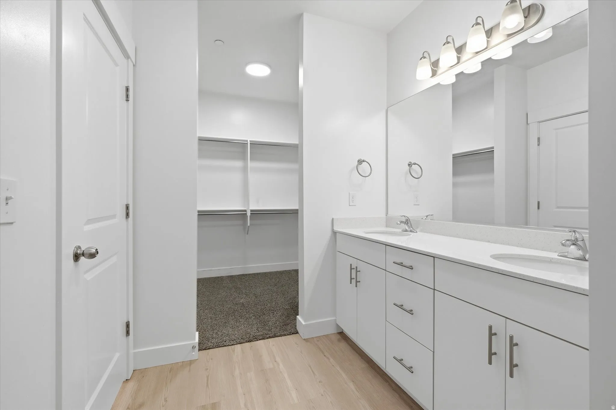 Double vanity featuring two integrated sinks, white cabinetry, chrome hardware, and a single large mirror