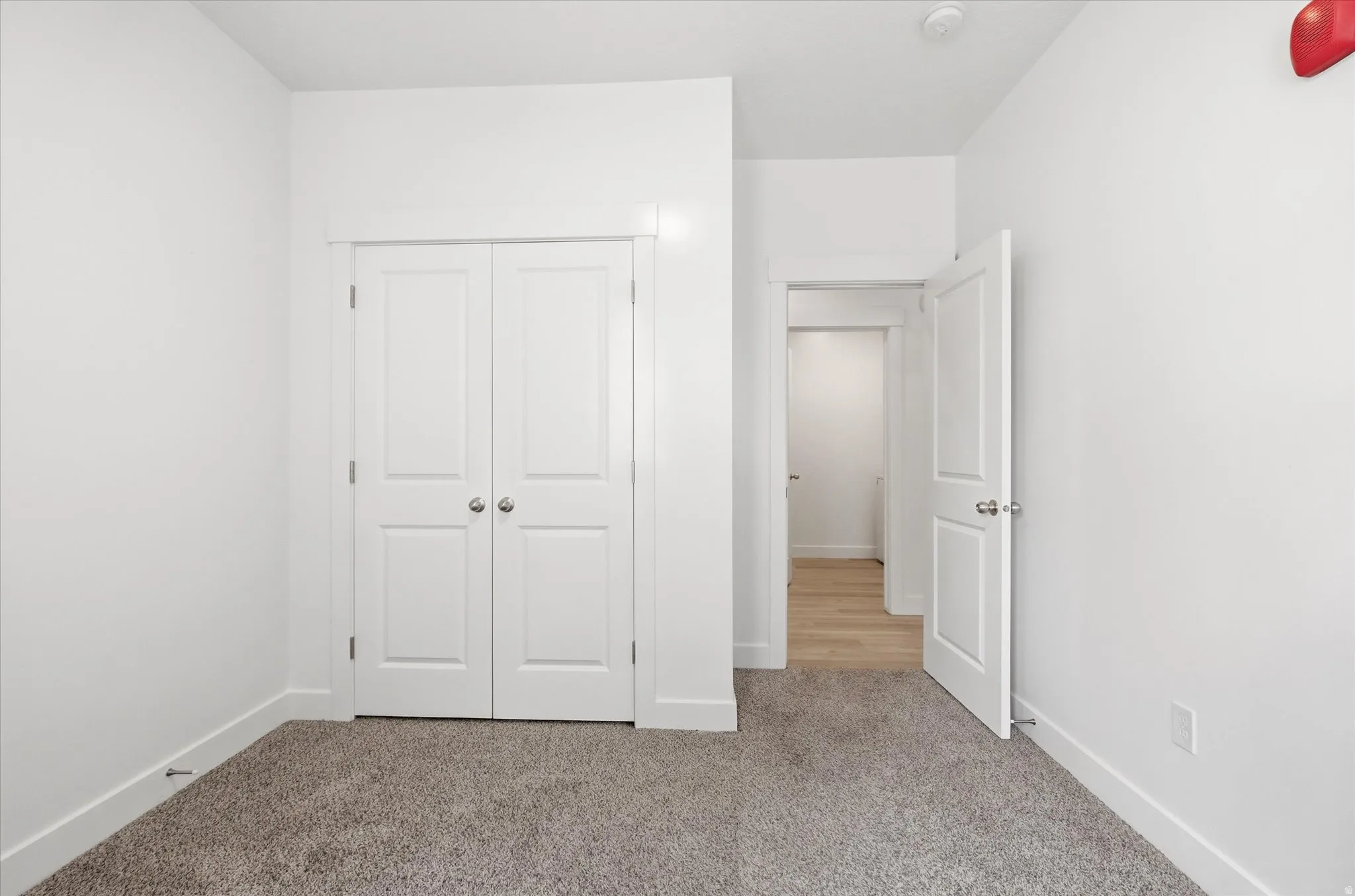 Interior room featuring neutral-toned carpeting, white baseboards, and a white interior door with brushed metal hardware