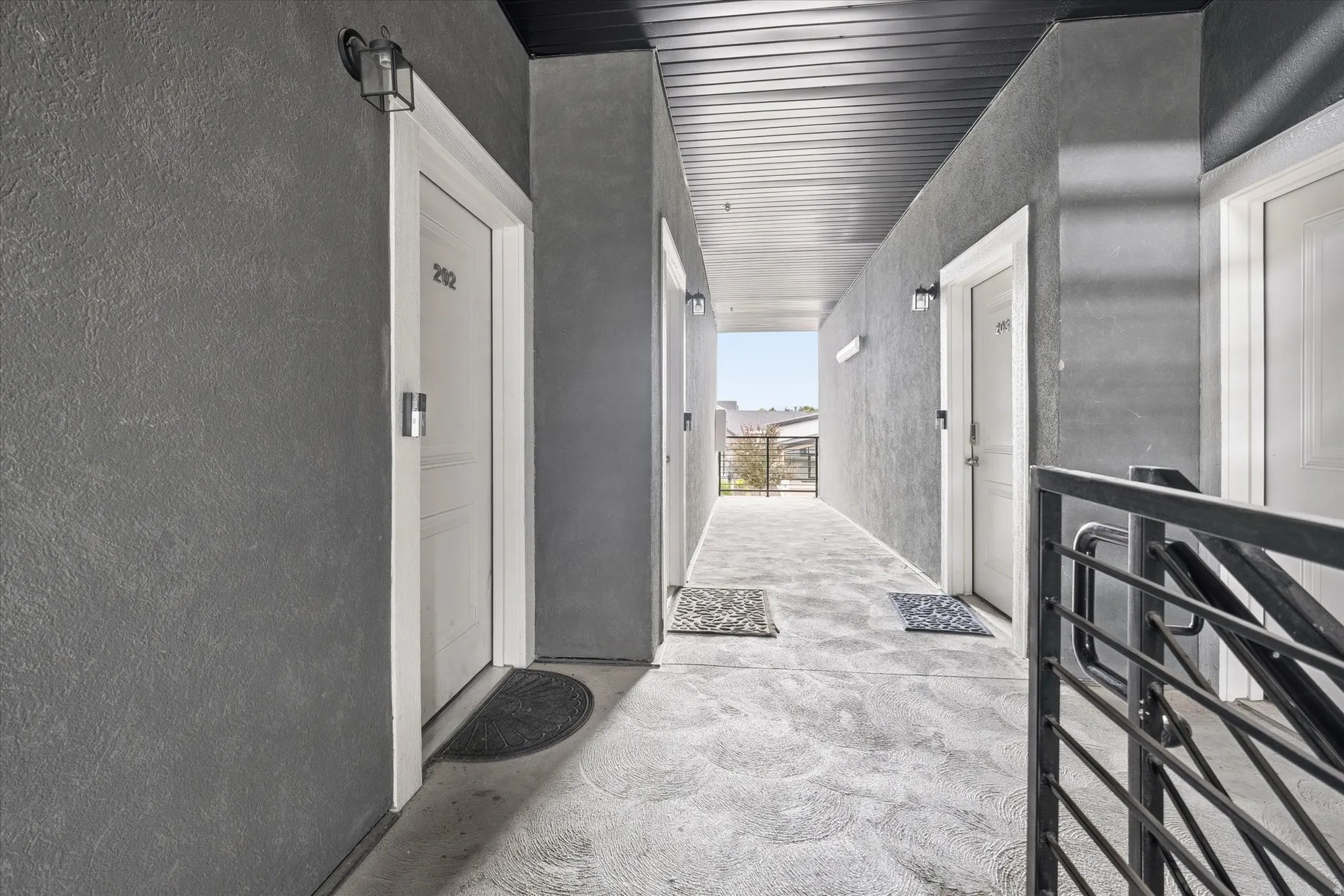 Exterior hallway featuring textured gray walls, white door trim, and a slatted black ceiling
