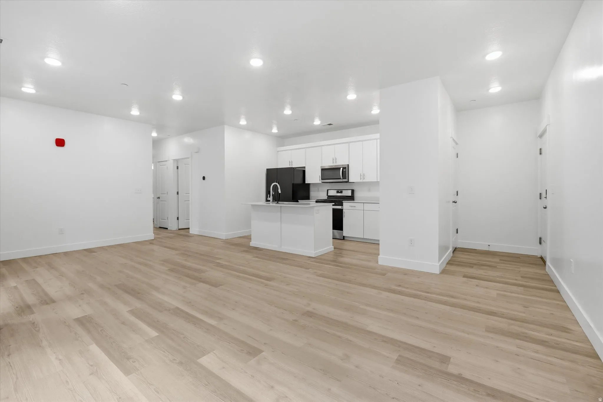 Open-concept living space featuring wood-finish flooring, recessed lighting, a white kitchen island with an integrated sink, white cabinetry, and stainless steel appliances