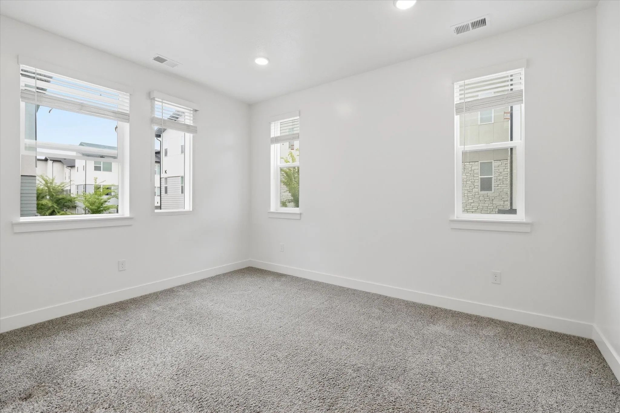 Bright interior space featuring light gray carpet, white walls, multiple windows with blinds, white trim, and recessed lighting