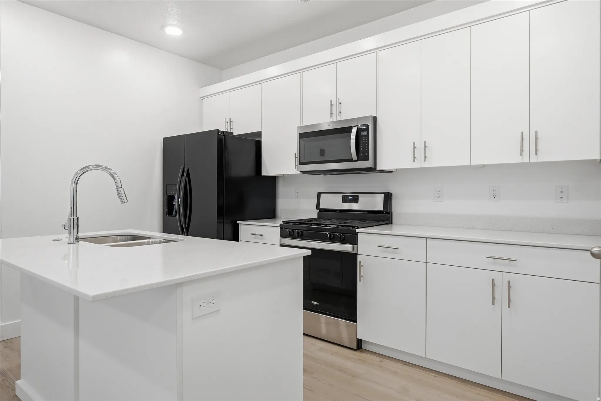 Contemporary kitchen featuring white cabinetry, light-toned countertops, a stainless steel gas range, and a kitchen island with an integrated sink and chrome faucet