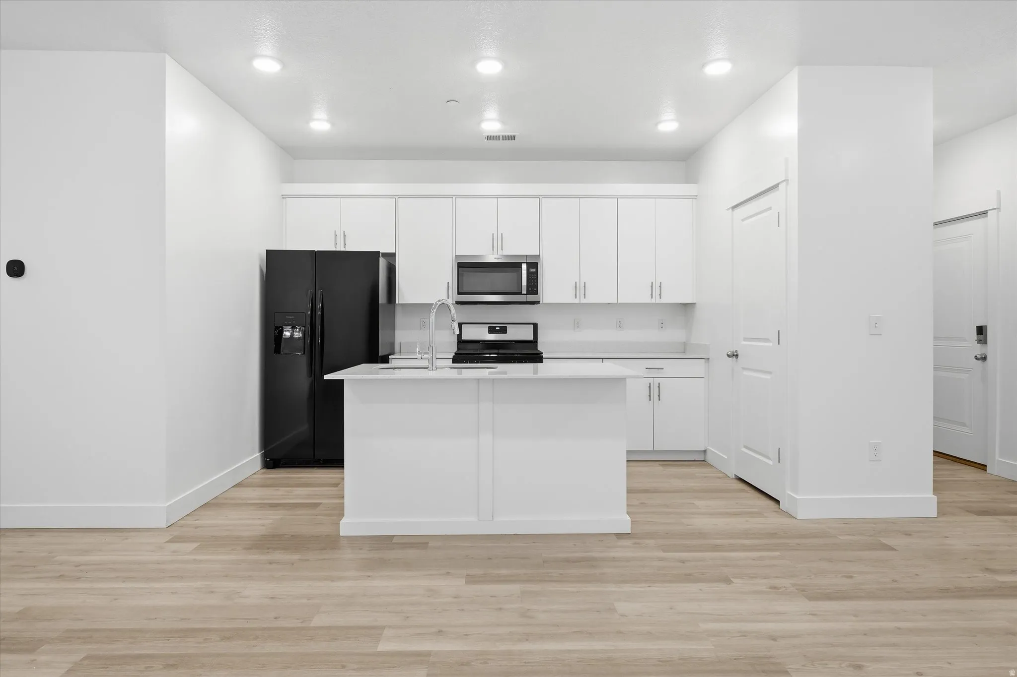 Modern kitchen featuring white cabinetry, a center island with sink, black appliances, recessed lighting, and light wood-finish flooring