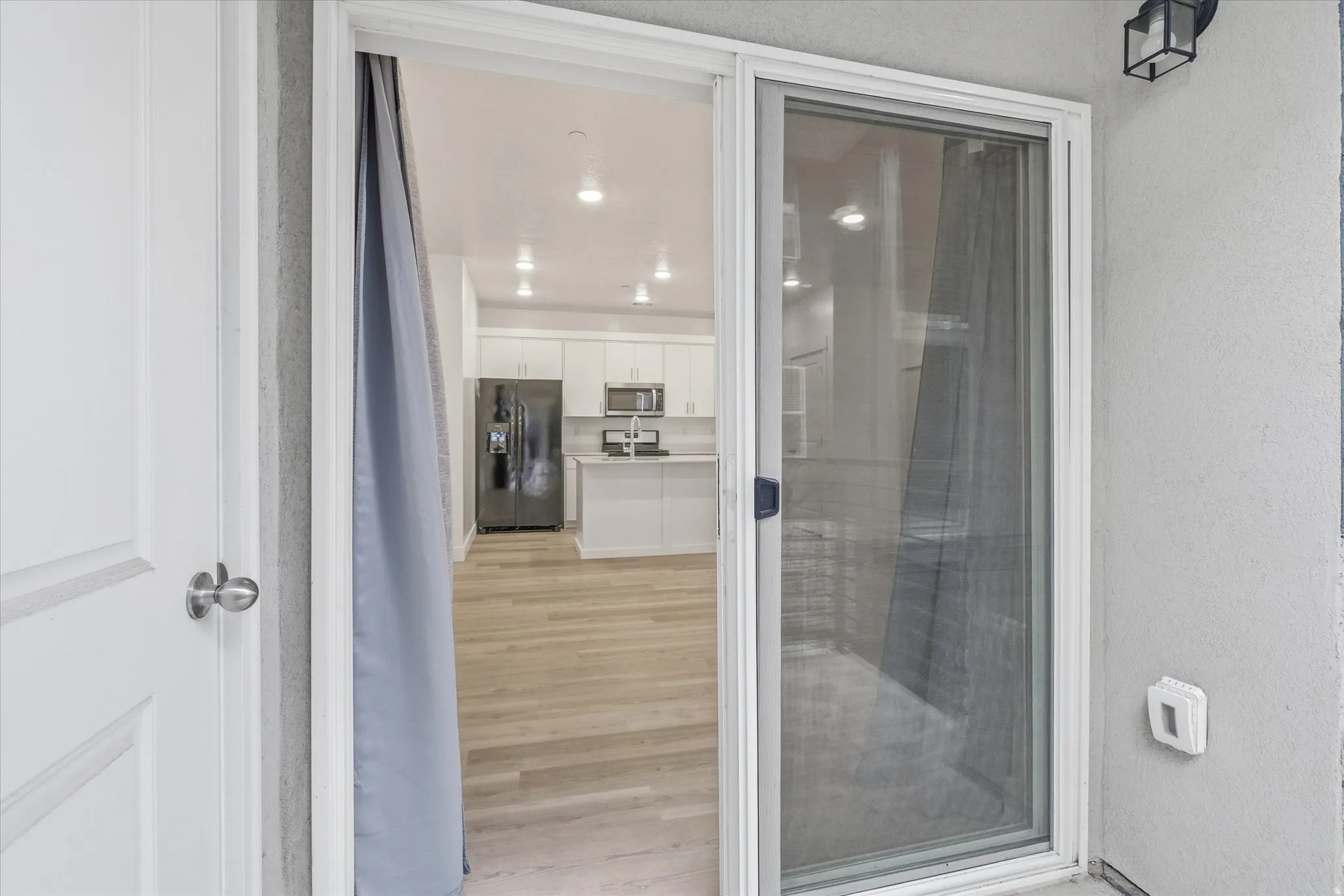 Sliding glass door opening to a modern kitchen featuring white cabinetry, stainless steel appliances, a center island with countertop seating, and recessed lighting