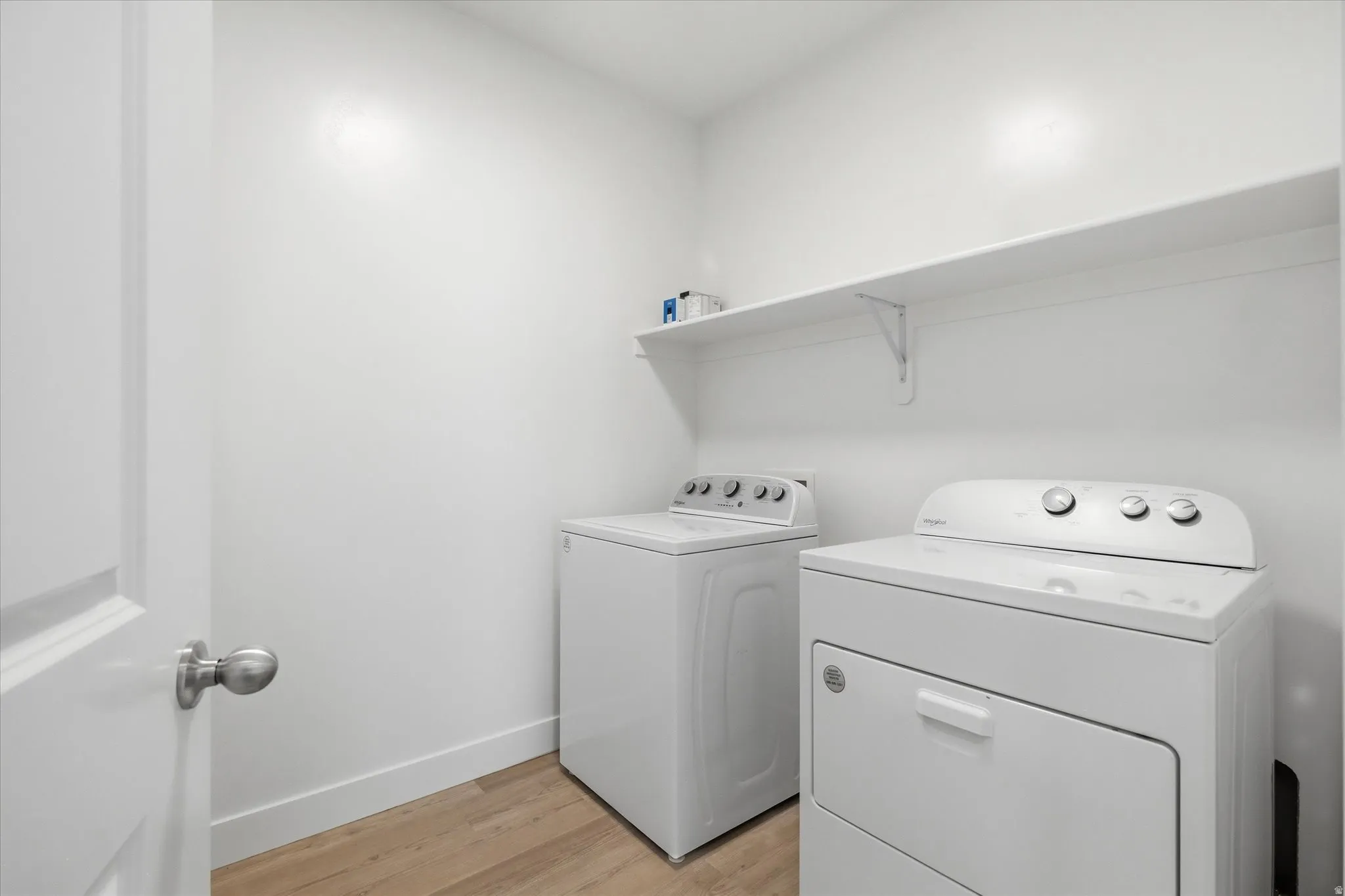 Dedicated laundry space featuring a floating shelf, light wood-finish flooring, and white baseboards