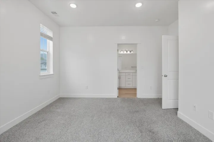 Spacious room featuring neutral carpeting, a large window with blinds, recessed ceiling lighting, and crisp white walls