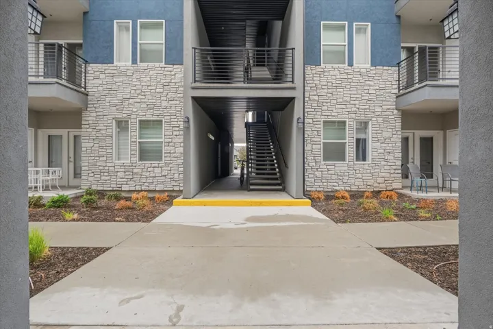 Multi-story building exterior featuring stone-look facade accents, balconies with black metal railings, and a prominent exterior staircase