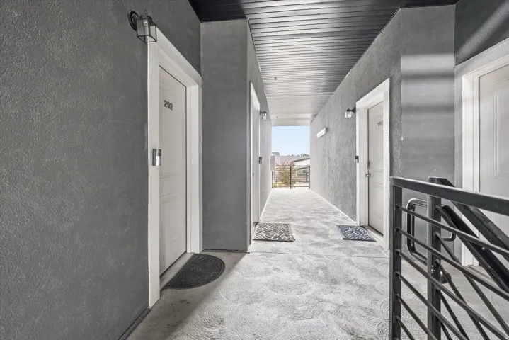 Exterior hallway featuring textured gray walls, white door trim, and a slatted black ceiling