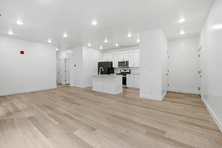Open-concept living space featuring wood-finish flooring, recessed lighting, a white kitchen island with an integrated sink, white cabinetry, and stainless steel appliances