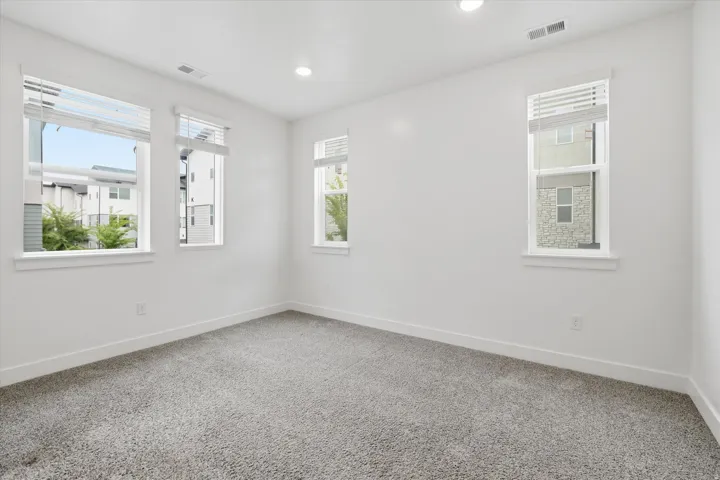 Bright interior space featuring light gray carpet, white walls, multiple windows with blinds, white trim, and recessed lighting
