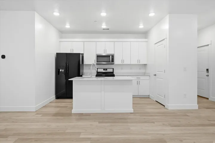Modern kitchen featuring white cabinetry, a center island with sink, black appliances, recessed lighting, and light wood-finish flooring