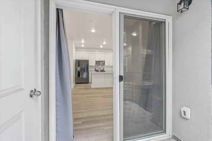 Sliding glass door opening to a modern kitchen featuring white cabinetry, stainless steel appliances, a center island with countertop seating, and recessed lighting