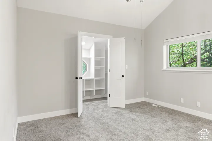 Carpeted interior room featuring a vaulted ceiling and a window with white trim