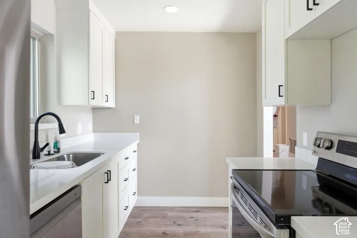 Kitchen featuring white cabinetry with dark hardware, a stainless steel sink with a dark faucet, white countertops, and wood-finish flooring