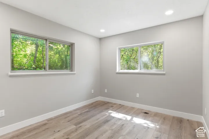 Room featuring two windows with white trim, light gray walls, wood-finish flooring, white baseboards, and recessed ceiling lighting