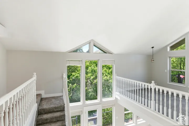 Loft area featuring vaulted ceilings, a contemporary pendant light fixture, and multiple large windows