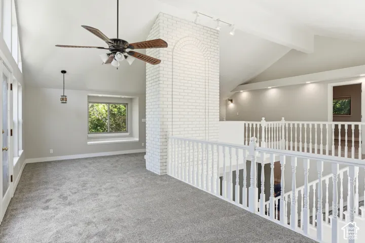 Carpeted loft area featuring a vaulted ceiling with a ceiling fan, a white painted brick architectural element, and a window with a deep sill