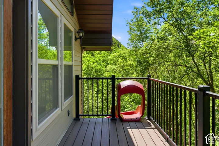 Exterior balcony featuring composite decking, black metal railings, and a wall-mounted light fixture