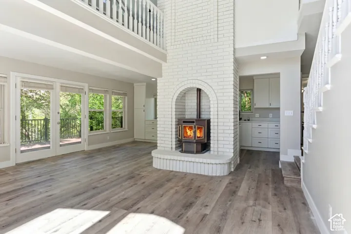 Two-story living space featuring a white brick fireplace with hearth, wood-finish flooring, and a second-story balcony with white balusters