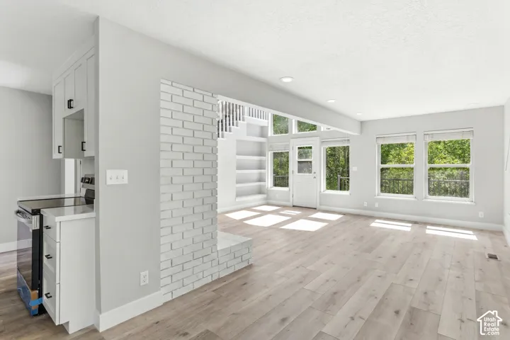 Open-concept living area with light wood-finish flooring, a white painted brick fireplace, and extensive window-framing