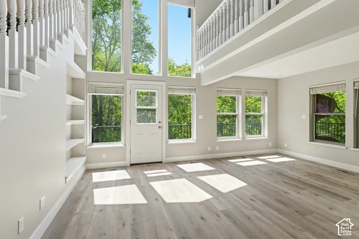 Two-story living area featuring extensive natural light, light wood-finish flooring, built-in shelving, a full-lite exterior door, and a second-story overlook with a white spindle railing