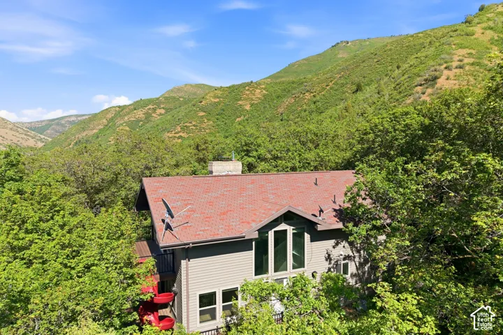 House with a red shingle roof, light gray siding, and a prominent window wall, nestled among mature green trees