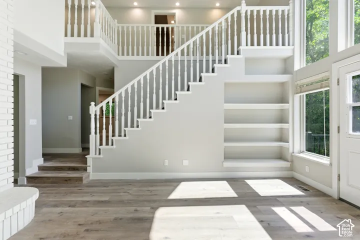 Grand entryway featuring a multi-level staircase with white balusters, wood-finish flooring, recessed lighting, built-in shelving, and a large window with natural light