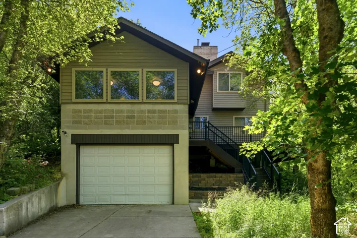 Multi-level residence featuring a prominent garage with a white panel door, a concrete driveway, and a retaining wall