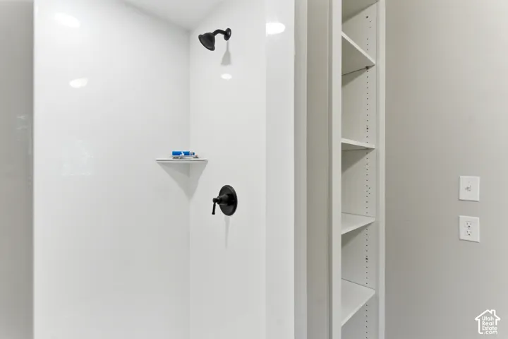 White shower stall with matte black fixtures, built-in corner shelf, and recessed lighting