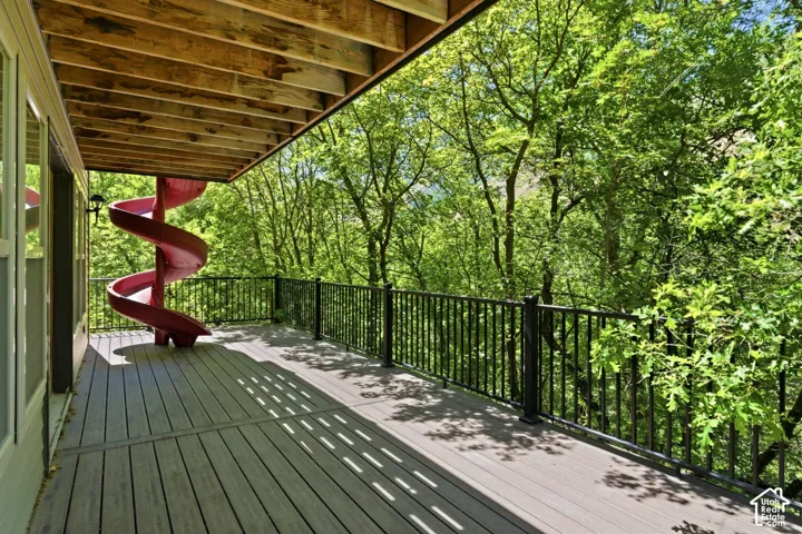 Spacious outdoor deck featuring composite decking, black metal railings, a spiral slide, and natural tree surroundings