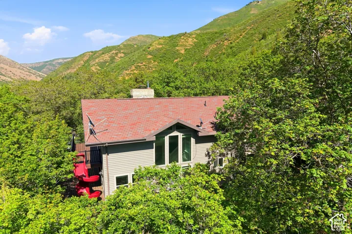 Mountain-surrounded residence featuring a red shingle roof, light-toned siding, and prominent windows