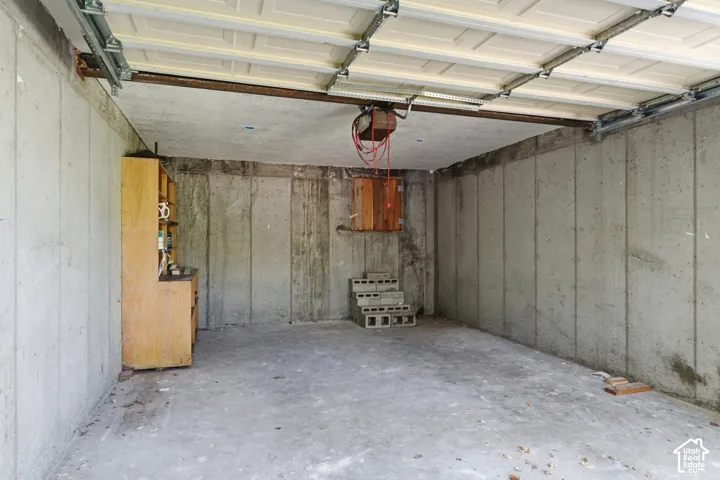 Concrete garage featuring an overhead door mechanism, built-in wooden cabinetry, and durable concrete walls