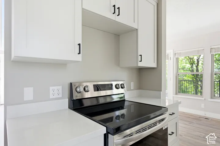 Kitchen area featuring white shaker cabinetry with matte black hardware, white countertops with a matching backsplash, and a stainless steel and black electric range
