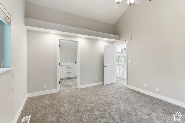 Spacious room featuring vaulted ceilings, neutral-toned carpeting, and a white trim package