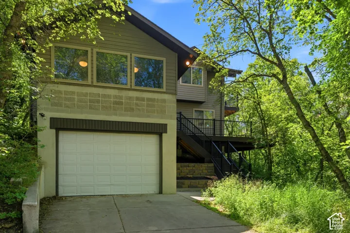 Contemporary two-story exterior featuring a prominent white garage door, upper-level rectangular windows, a multi-level deck with black railings, and a concrete block foundation