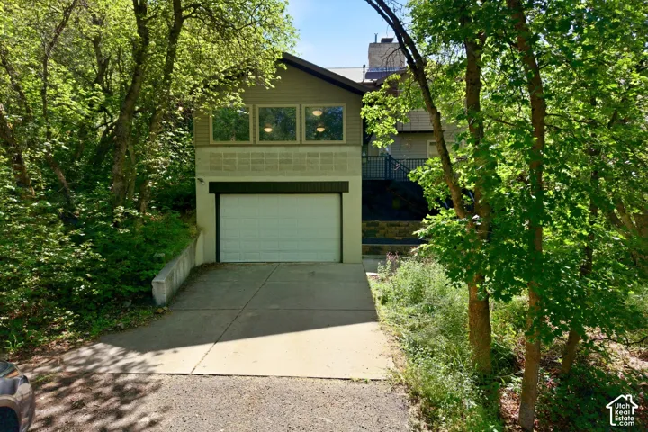 Multi-level property exterior featuring a white garage door, concrete driveway, and a retaining wall