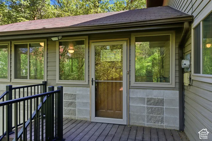 Exterior entryway featuring a wood-panel door with storm door, composite decking, black metal railing, and concrete block accents