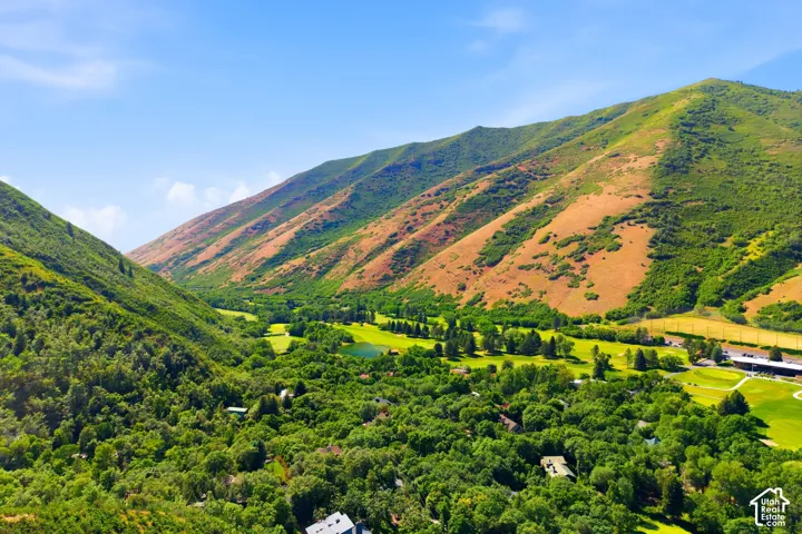Expansive mountain landscape featuring lush green peaks, a verdant valley, a golf course with a central water feature, and substantial tree coverage