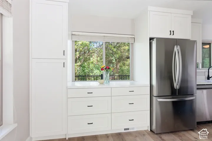 Kitchen featuring white shaker cabinetry, stainless steel French door refrigerator, white solid surface countertops, wood-finish flooring, and a large window