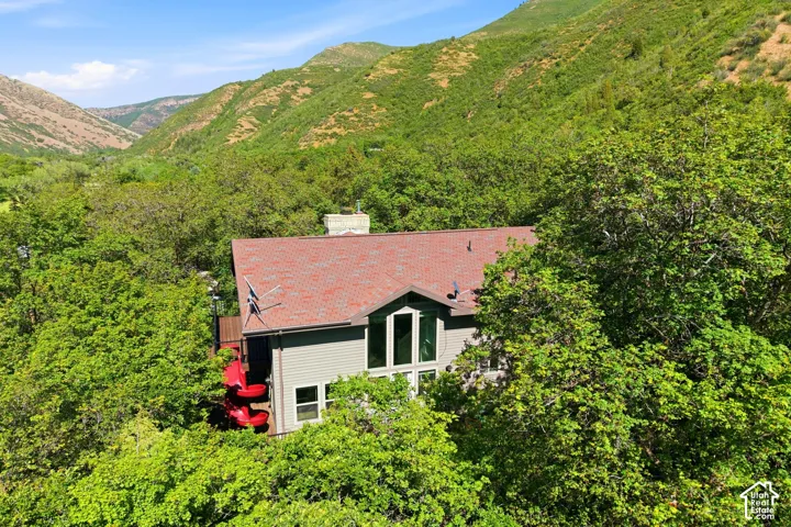 Property featuring a red roof and pale gray siding, surrounded by abundant mature trees