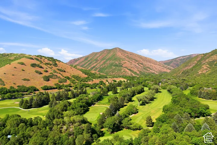 Expansive golf course setting featuring manicured fairways and mature trees, surrounded by mountainous terrain and natural landscaping