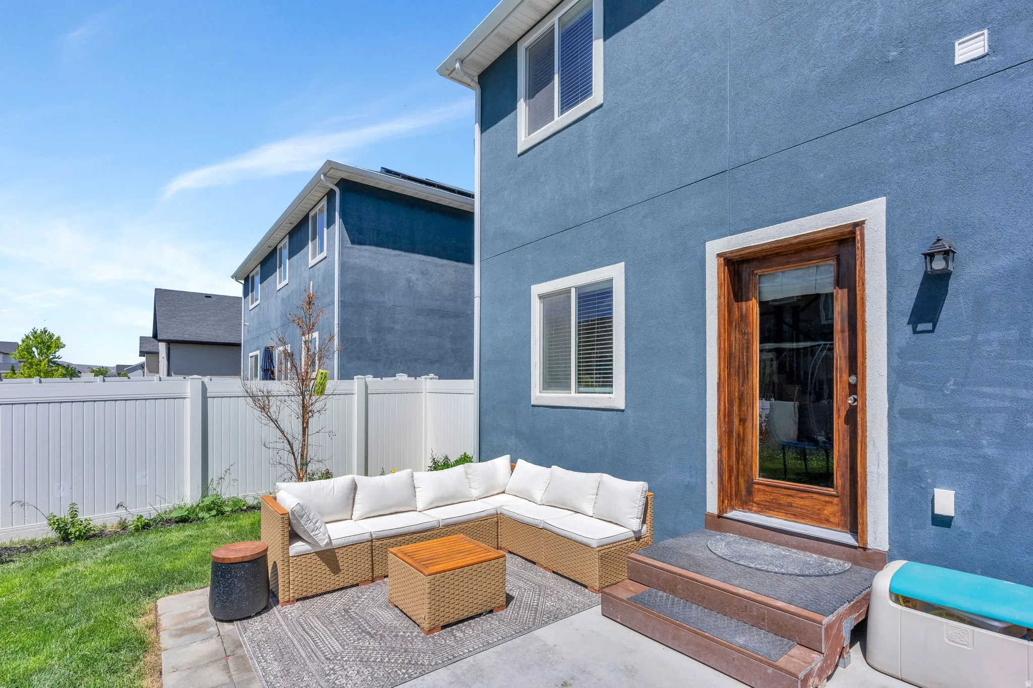 Exterior patio space with a concrete slab, a manicured lawn, and a white privacy fence
