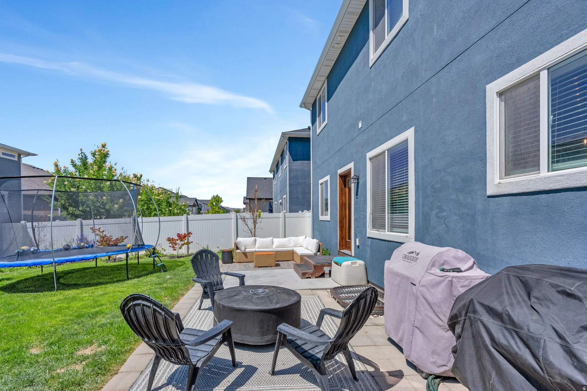 Expansive backyard featuring a paver patio, a separate concrete patio area, and a green lawn bordered by a white privacy fence
