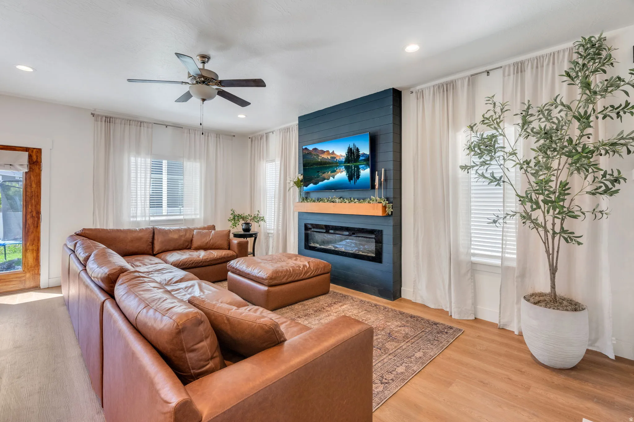 Living room featuring a prominent shiplap accent wall with an electric fireplace, wood-finish flooring, recessed lighting, and a ceiling fan