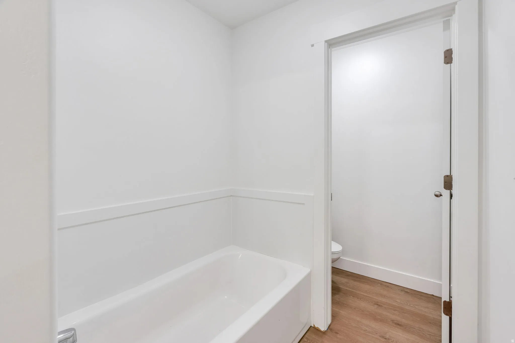 Bright white bathtub with wainscoting detail and wood-finish flooring