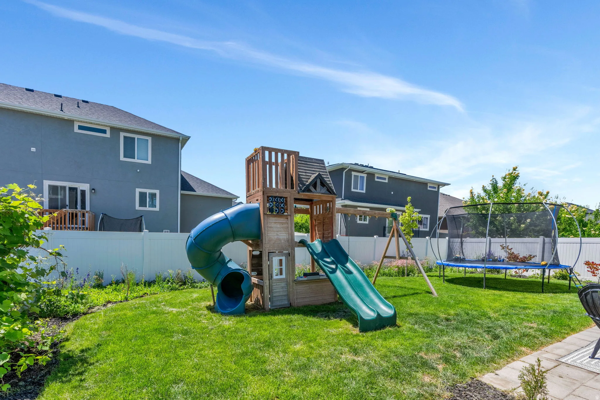 Expansive backyard featuring a manicured lawn, a wooden playset with a tube slide, and a paved patio area