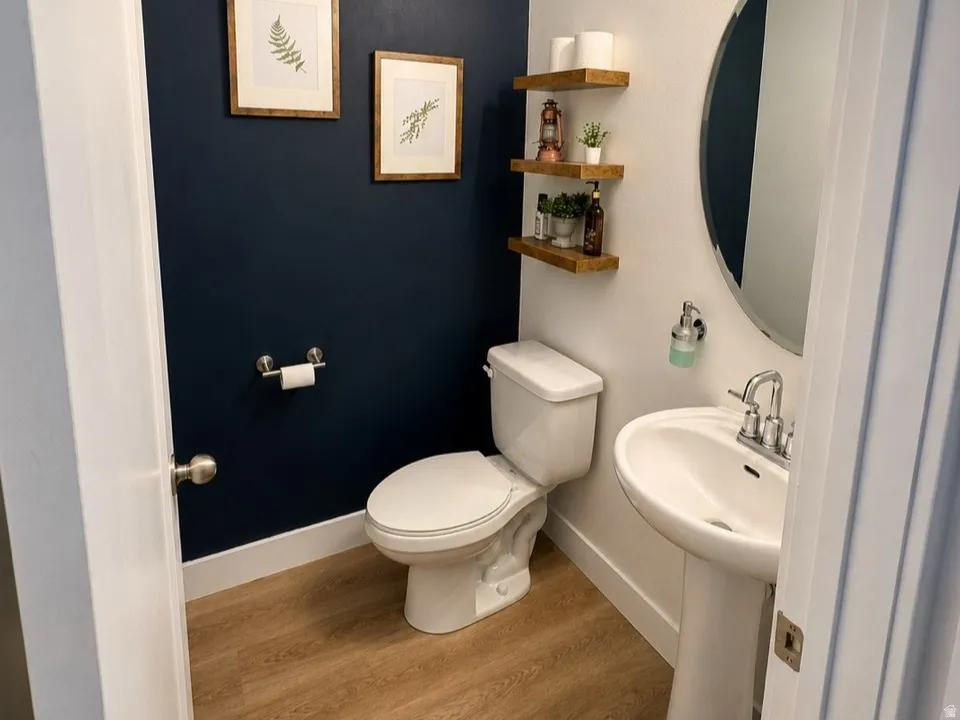 Powder room featuring a pedestal sink, round wall mirror, wood-finish flooring, and a two-light vanity fixture