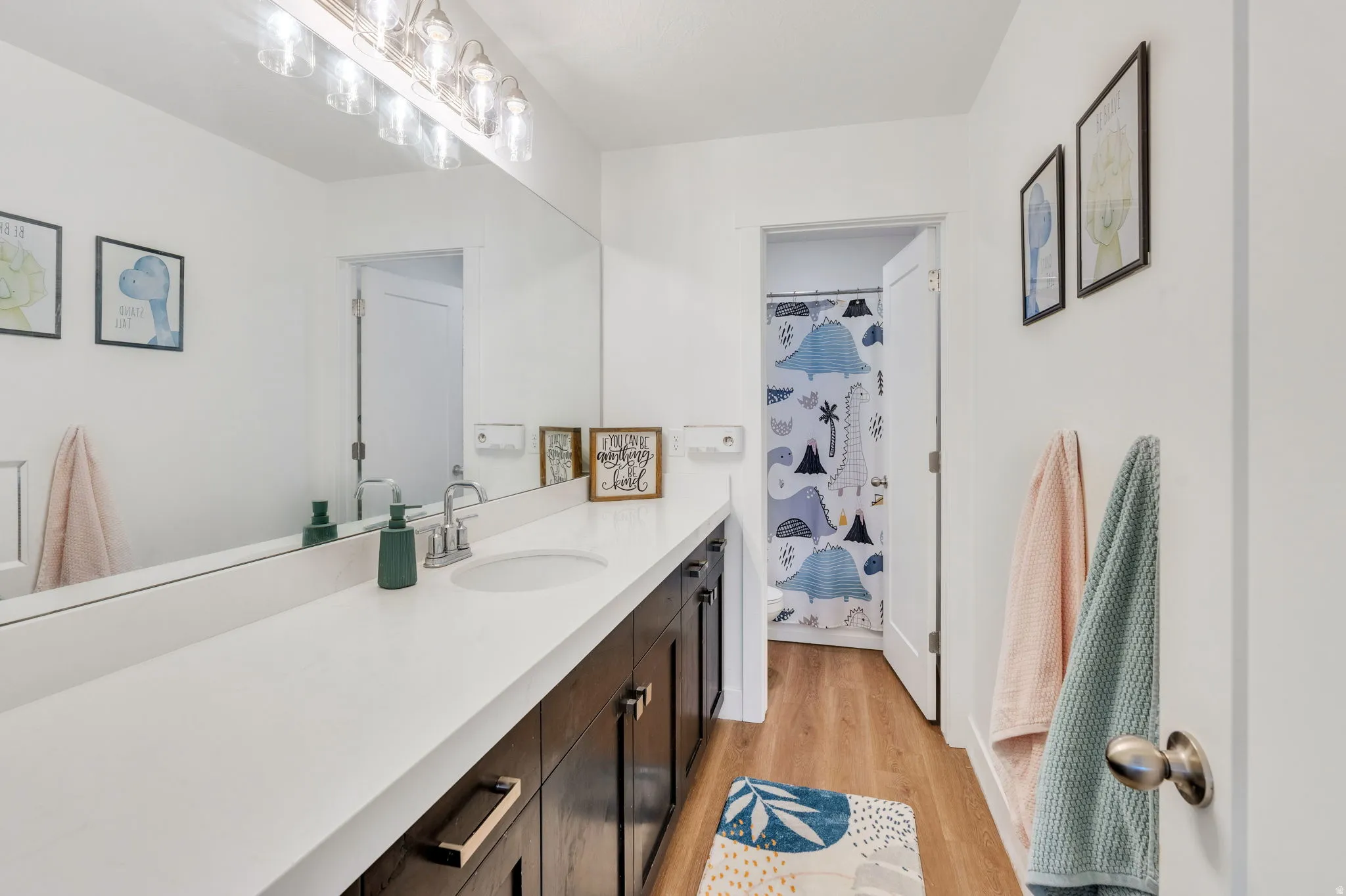 Modern bathroom featuring a long vanity with a single integrated sink, a large wall-mounted mirror, and overhead vanity lighting