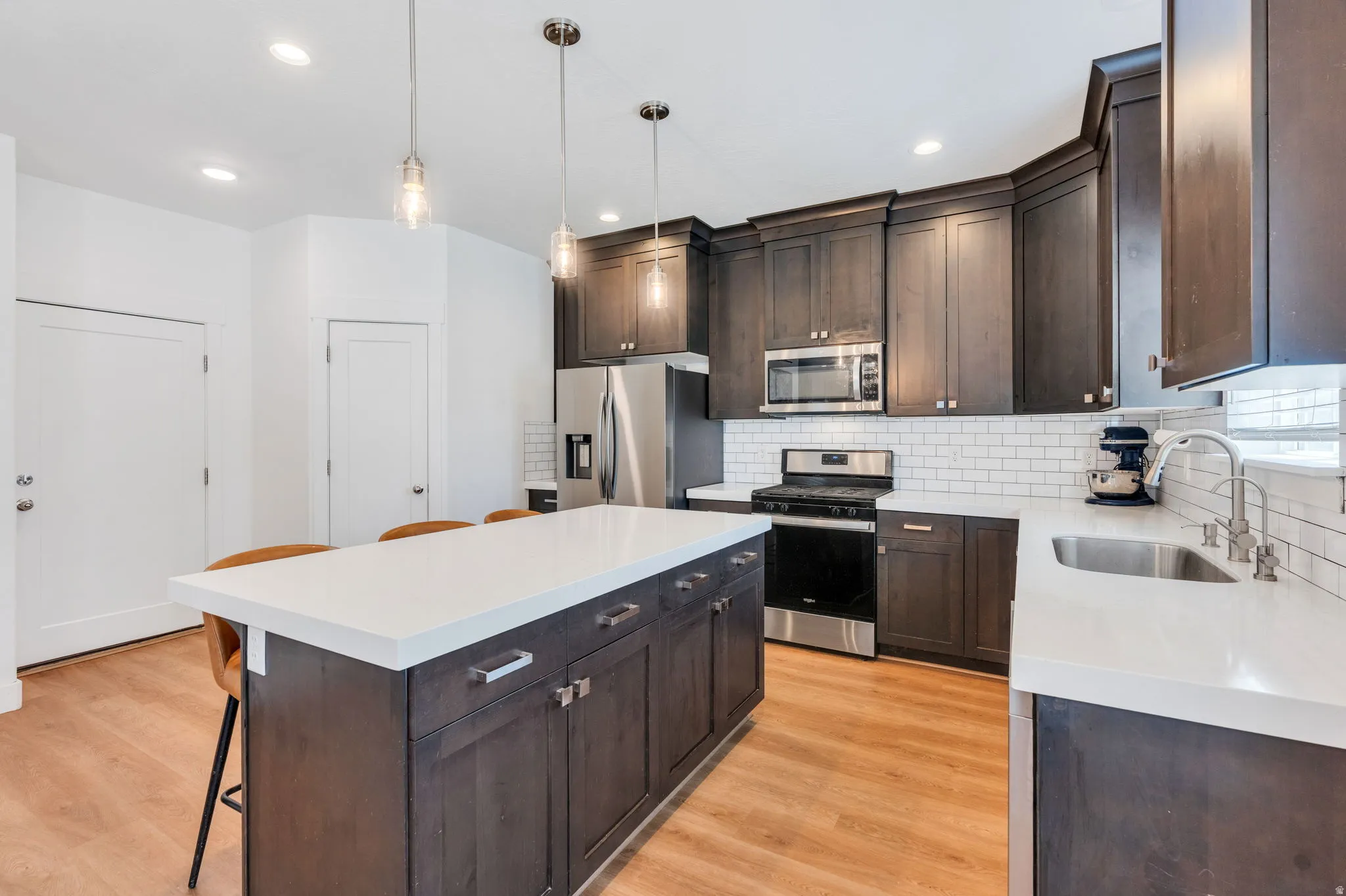 Kitchen featuring a central island with white countertop, dark wood-finish cabinetry, stainless steel appliances, white subway tile backsplash, and wood-finish flooring